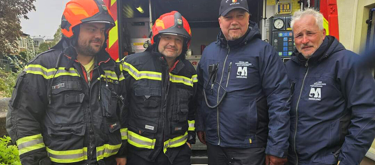 Vier Männer in Feuerwehruniform vor einem Einsatzfahrzeug.